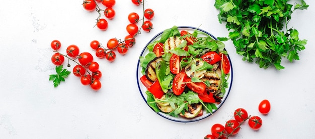Gesunder veganer Salat mit gegrilltem Gemüse Paprika-Zucchini-Auberginen mit frischen Tomaten und gemischten Kräutern Draufsicht auf den weißen Tischhintergrund