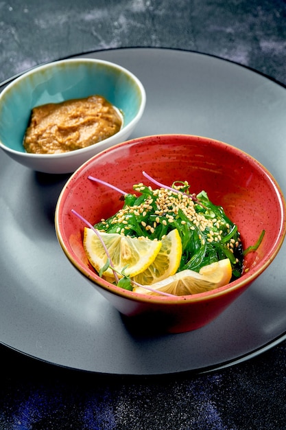 Gesunder Wakame-Seetang-Salat mit Erdnusssauce auf schwarzem Hintergrund. Nahansicht