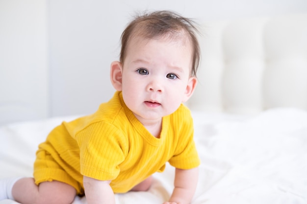 Gesundes asiatisches Mädchen 5 Monate im gelben Bodysuit auf dem Bett auf weißer Bettwäsche