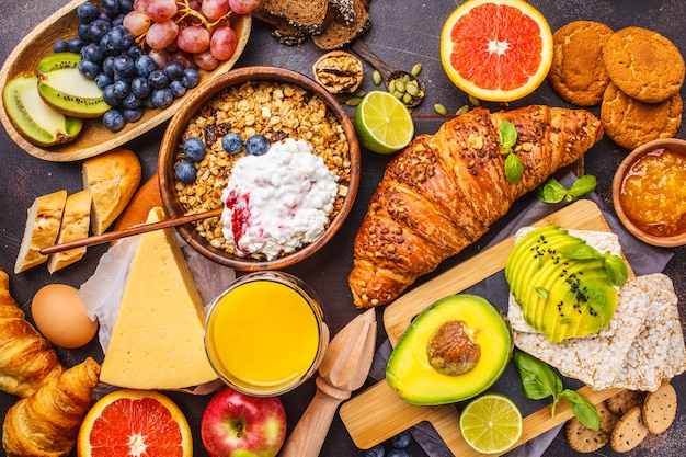 Gesundes ausgeglichenes Frühstück auf einem dunklen Hintergrund. Müsli, Milch, Saft, Croissants, Käse, Kekse.