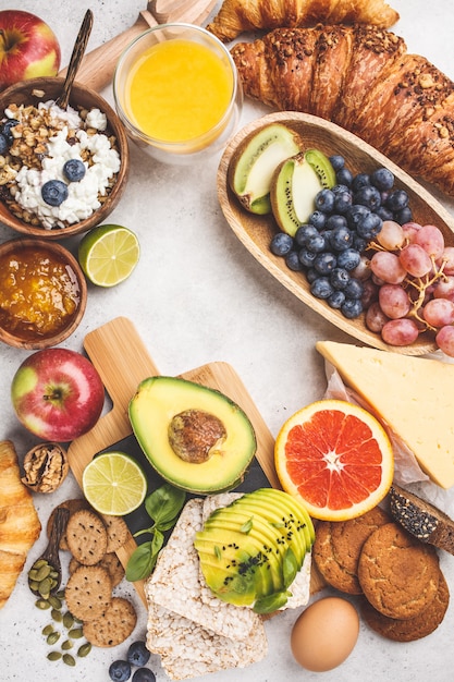 Gesundes ausgeglichenes Frühstück auf weißem Hintergrund. Müsli, Saft, Croissants, Käse, Kekse und Obst, Draufsicht.