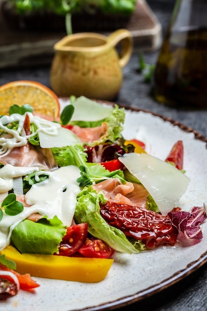 Gesundes ausgewogenes Mittagessen, geräucherter Lachs, Salat, sonnengetrocknete Tomaten und Käsesauce, vertikales Bild. Ansicht von oben.