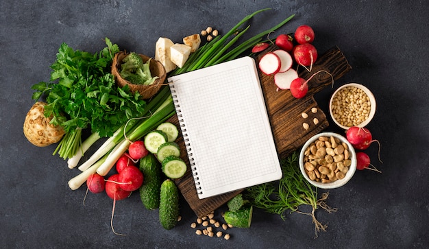 Gesundes ausgewogenes veganes Lebensmittelkonzept. Leeres Notizbuch mit frischem Gemüse, Kräutern, Müsli und Nüssen. Veggie kochen