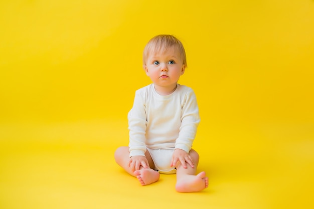 Gesundes Baby im weißen Bodysuit sitzt auf gelbem Hintergrund, Raum für Text
