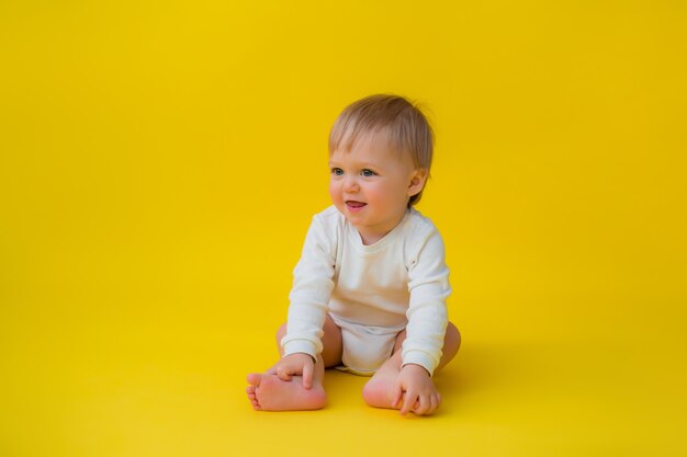 Gesundes Baby im weißen Bodysuit sitzt auf gelbem Hintergrund, Raum für Text