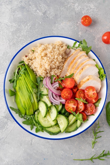 Gesundes Bowl-Mittagessen mit gegrilltem Hühnchen, Quinoa, Avocado, Tomaten, Gurken und frischem Rucola