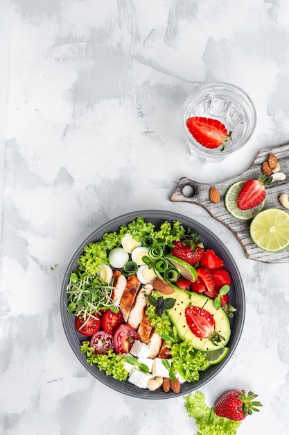 Gesundes Buddha-Bowl-Mittagessen mit gegrilltem Hühnchen und Avocado, Feta-Käse, Wachteleiern, Erdbeeren, Nüssen und Salat. Köstliches ausgewogenes Lebensmittelkonzept. vertikales Bild. Ansicht von oben. Platz für Text.