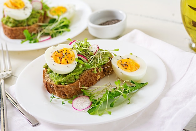 Gesundes Essen. Frühstück. Avocado-Ei-Sandwich mit Vollkornbrot auf weißer Holzoberfläche.