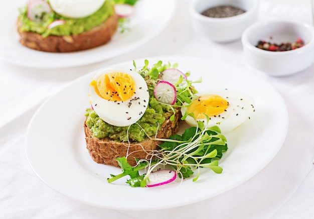 Gesundes Essen. Frühstück. Avocadoei-Sandwich mit Vollkornbrot auf weißem hölzernem Hintergrund.