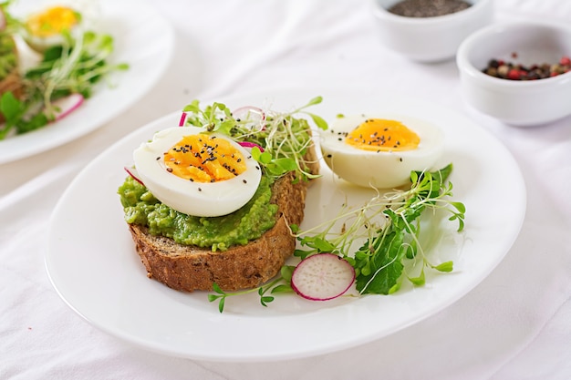 Gesundes Essen. Frühstück. Avocadoeisandwich mit Vollkornbrot auf weißem Holztisch.