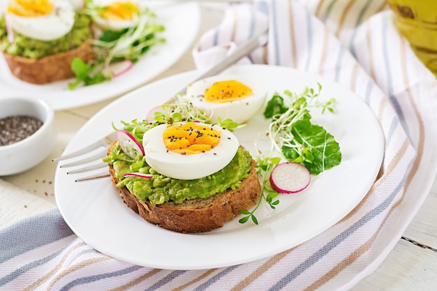 Gesundes Essen. Frühstück. Avocadoeisandwich mit Vollkornbrot auf weißem Holztisch.