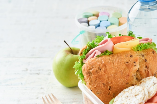 Gesundes Essen für das Schulessen-Konzept. Gesundes Brot-Fleisch-Sandwich mit Käse, Apfel, frischen Gurken, Karotten, Nüssen im Behälter, Wasser und Joghurt auf Küchenhintergrund. Zurück zum Schulkonzept