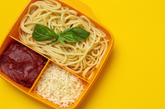 Gesundes Essen in Plastikbehältern essfertig mit hausgemachten Spaghetti mit Tomaten, Käse und Basilikum auf dem Arbeitstisch. Italienisches Essen. Wegnehmen.