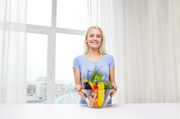Gesundes Essen, Kochen, vegetarisches Essen, Diäten und People-Konzept - lächelnde junge Frau mit Schüssel Gemüse zu Hause