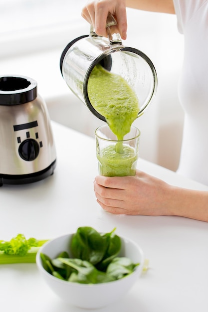 Gesundes Essen, Kochen, vegetarisches Essen, Diäten und People-Konzept - Nahaufnahme einer jungen Frau mit grünem Gemüse, die zu Hause Detox-Shake oder Smoothie aus dem Mixbecher ins Glas gießt