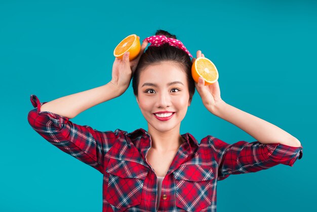 Gesundes Essen. Lächelndes reizendes asiatisches Pinupmädchen, das Orange über blauem Hintergrund hält.