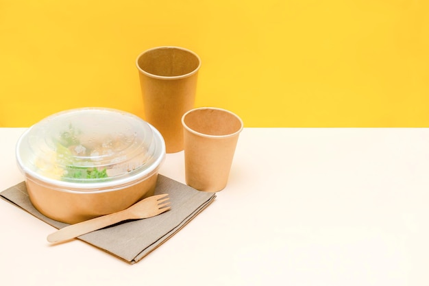 Gesundes Essen Mittagessen in Kraftpapier Karton umweltfreundliche Box Einwegschüssel Verpackungsbehälter, Tasse auf gelbem Hintergrund. Lieferung zum Mitnehmen. Kopierraum für den Umweltschutz