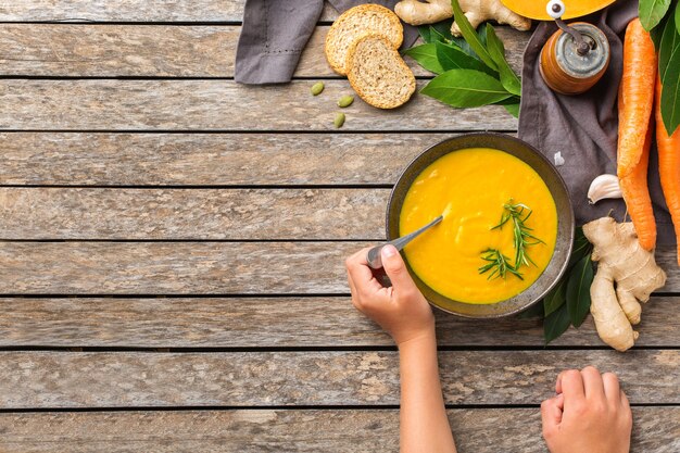 Gesundes Essen, sauberes Essenskonzept. Saisonale würzige Herbstgemüse cremige Kürbis- und Karottensuppe mit Zutaten auf einem rustikalen Holztisch. Flacher Laienhintergrund der Draufsicht mit Kinderkinderhänden