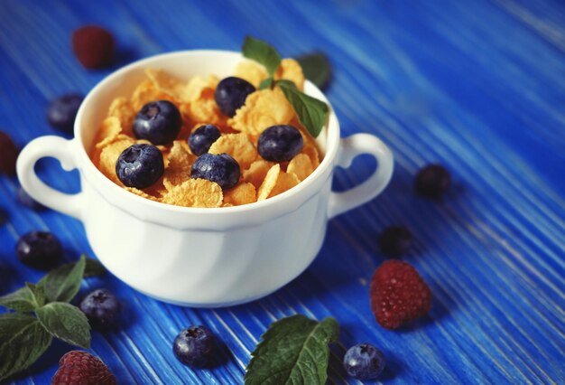 Gesundes Essen und Ernährungskonzept Cornflakes mit Beeren, Himbeeren und Heidelbeeren auf blauem Holzhintergrund