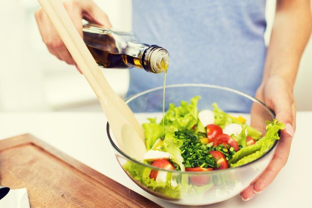 Gesundes Essen, vegetarisches Essen, Diäten und People-Konzept - Nahaufnahme einer jungen Frau, die zu Hause Gemüsesalat mit Olivenöl anzieht