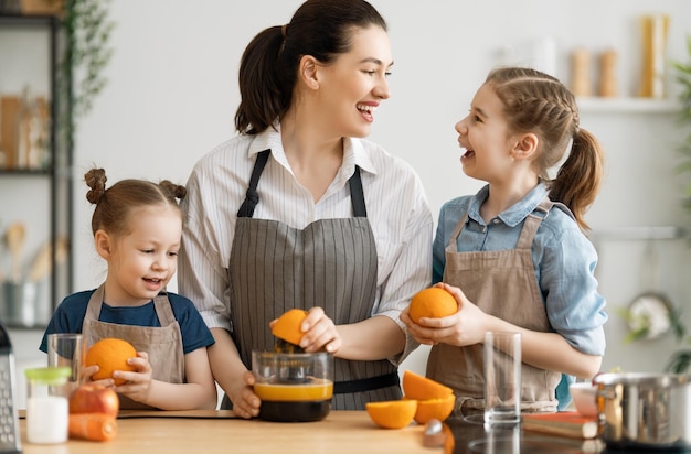 Gesundes Essen zu Hause. Glückliche Familie in der Küche. Mutter- und Kindertöchter bereiten frischen Orangensaft vor.