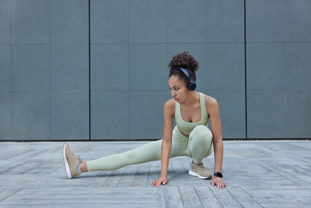 Gesundes Fitnessmodel in Sportkleidung streckt die Beine vor dem Training demonstriert ihre Flexibilität hört Musik in kabellosen Kopfhörern