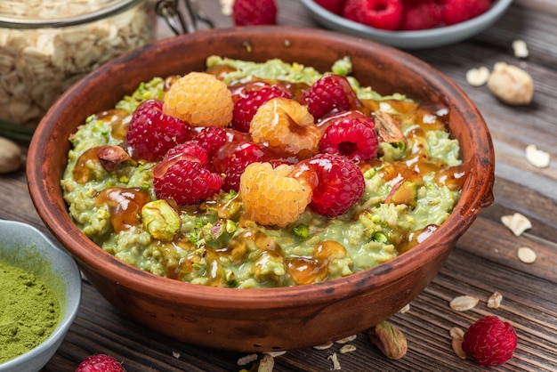 Gesundes Frühstück Haferflocken-Matcha-Brei mit frischer Himbeerkaramellsauce und Pistazien in einer Schüssel