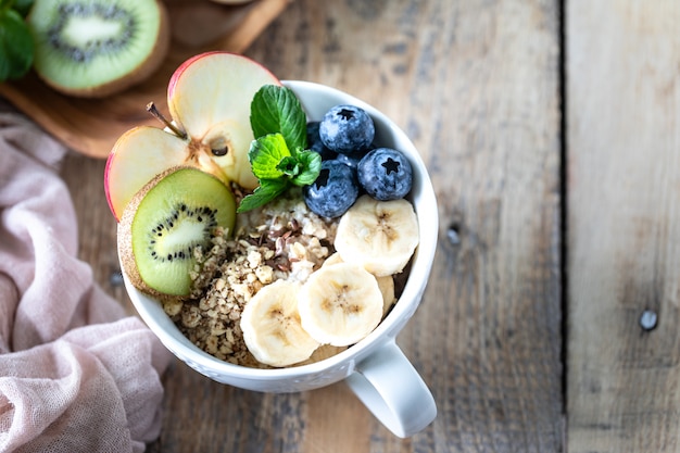 Gesundes Frühstück, Haferflocken oder Müsli mit Blaubeeren, Apfel, Kiwi und Minze auf einem rustikalen hölzernen Hintergrund. Nahansicht. Speicherplatz kopieren