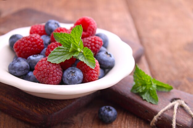 Gesundes Frühstück. Himbeeren und Blaubeeren in einer weißen Schüssel auf einem hölzernen Hintergrund.