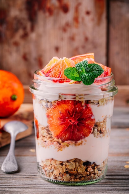 Gesundes Frühstück in einem Glas-Joghurt-Parfait mit hausgemachtem Müsli und Blutorange auf Holzhintergrund