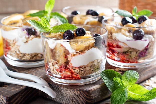 Gesundes Frühstück: Joghurtparfait mit Müsli, Banane und Blaubeere auf Holzuntergrund