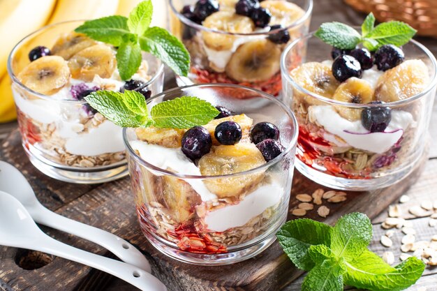 Gesundes Frühstück: Joghurtparfait mit Müsli, Banane und Blaubeere auf Holzuntergrund