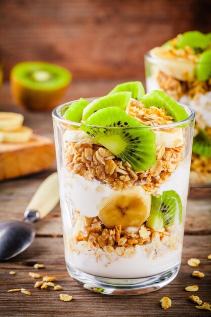 Gesundes Frühstück Joghurtparfait mit Müslibanane und Kiwi auf Holzhintergrund