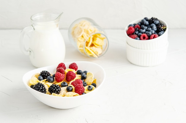 Gesundes Frühstück mit Cornflakes in einem weißen Teller, Beeren, Milch und Kaffee