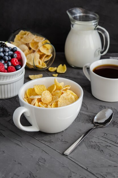 Gesundes Frühstück mit Cornflakes in einer weißen Tasse, Beeren, Milch und Kaffee