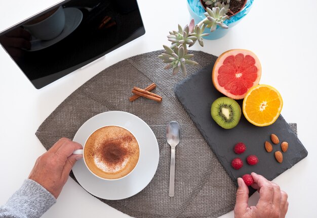 Gesundes Frühstück mit einem heißen hausgemachten Cappuccino und Zitrusfrüchten mit Mandeln. Pflanzen und Tablette