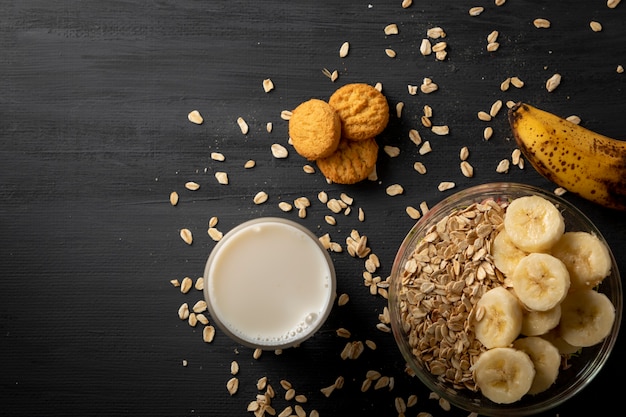 Gesundes Frühstück mit Haferflocken mit Banane ein Glas Milch und ein paar Kekse auf dem schwarzen Tisch