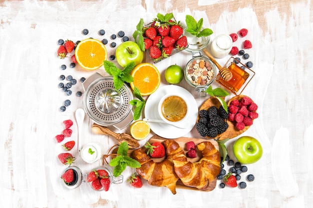 Gesundes Frühstück mit Kaffee, Croissants, Müsli, Milch, frischen Beeren, Früchten. Ansicht von oben