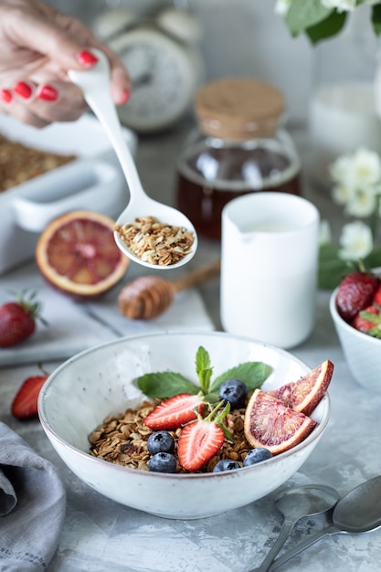 Gesundes Frühstück mit Müsli, Joghurt, Früchten, Beeren auf einem weißen Teller in weißem Teller.