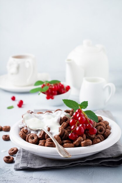 Gesundes Frühstück mit Schokoladenmaisringen, Beeren der roten Johannisbeere, Joghurt und Tee auf einem grauen Betonhintergrund Kopieren Sie Raum.