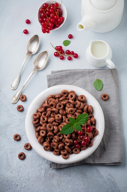 Gesundes Frühstück mit Schokoladenmaisringen, roten Johannisbeeren, Joghurt und Tee auf grauer Betonoberfläche