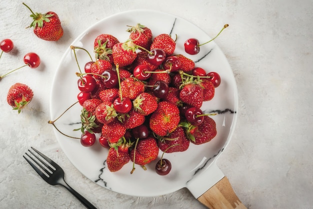 Gesundes Frühstück, Mittagessen oder Snack. Sommerbeeren und Früchte. Runde weiße Marmorplatte der organischen frischen Kirschen und der Erdbeeren, auf einer weißen Tabelle.