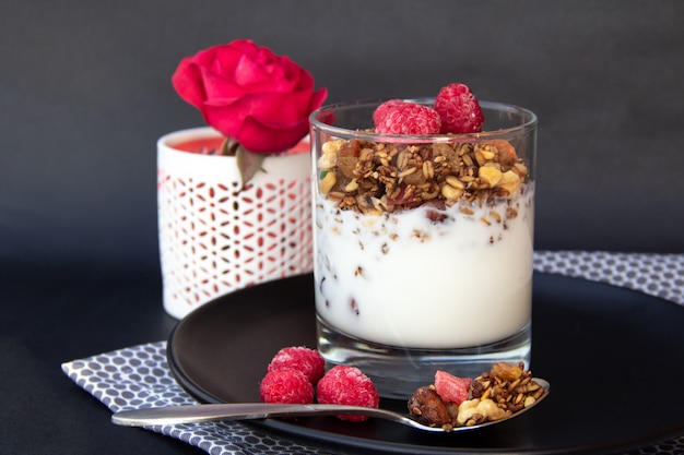 Gesundes Frühstück. Müsli mit Joghurt und Himbeeren auf schwarzem Teller.