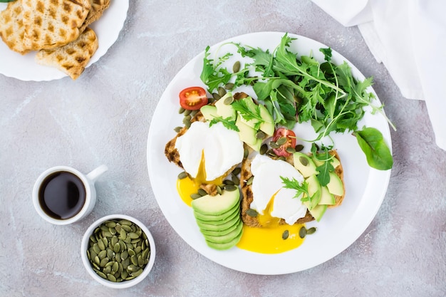 Gesundes Frühstück. Pochierte Eier auf Toast mit Avocadostücken, Rucola, Mizuna und Mangoldblättern und Kirschtomaten auf einem Teller auf einem servierten Tisch. Flexetarian-Diät. Ansicht von oben. Platz kopieren