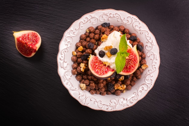 Gesundes Frühstück: Schüssel Schokoladenbälle mit Joghurt und frischen Feigen auf schwarzer Steintabelle.