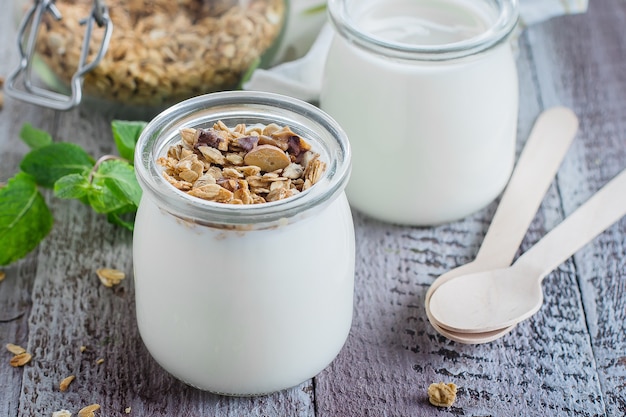 Gesundes Frühstück. Selbst gemachtes Hafergranola mit griechischem Joghurt und tadellosen Blättern auf hölzernem Hintergrund