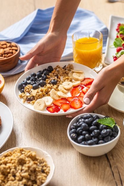 Gesundes Frühstück serviert mit einem Teller mit Joghurt-Müsli-Heidelbeeren, Erdbeeren und Banane. Morgentisch Müsli Mandeln Beeren Zitrusfrüchte Saft Kaffee Croissants und grüne Kräuter.