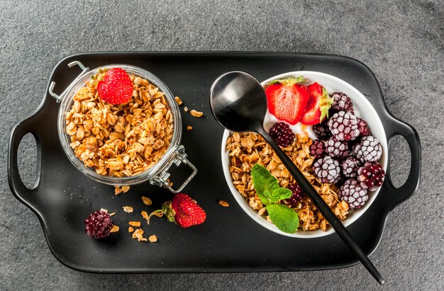 Gesundes Frühstück. Sommerbeeren und Früchte. Selbst gemachter griechischer Joghurt mit Granola, Brombeeren, Erdbeeren und Minze. schwarzer Steintisch, mit den Zutaten. Ansicht von oben