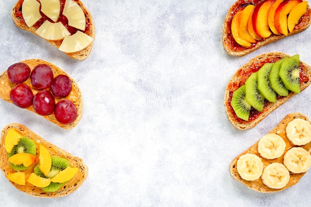 Gesundes frühstück toast mit erdnussbutter, erdbeermarmelade, banane, trauben, pfirsich, kiwi, ananas, nüssen. speicherplatz kopieren