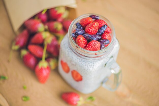 Gesundes geschichtetes Dessert mit Chia-Pudding, Erdbeere und Geißblatt in einem Einmachglas auf rustikalem Hintergrund.